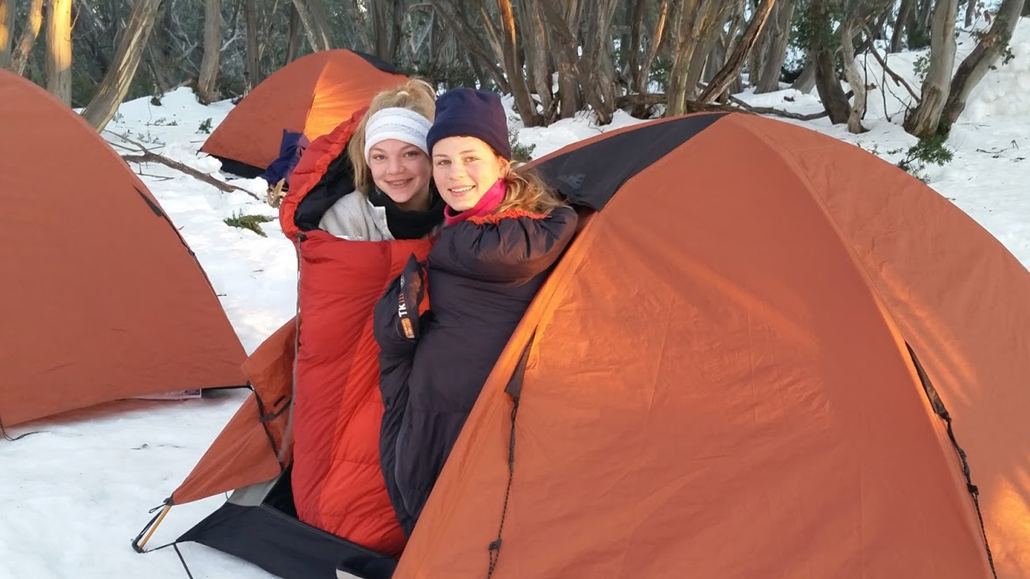 Two girls in sleeping bags poking their heads out of a tent